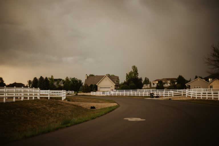 Storm clouds over homes behind a white rail fence