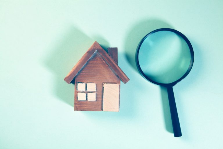 Magnifying glass beside a small wooden house model